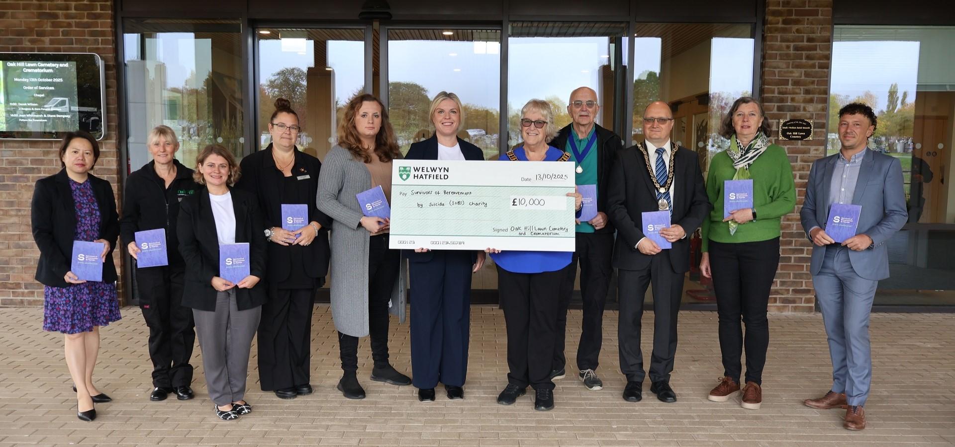 people standing next to someone holding a £10,000 cheque for the soBS charity