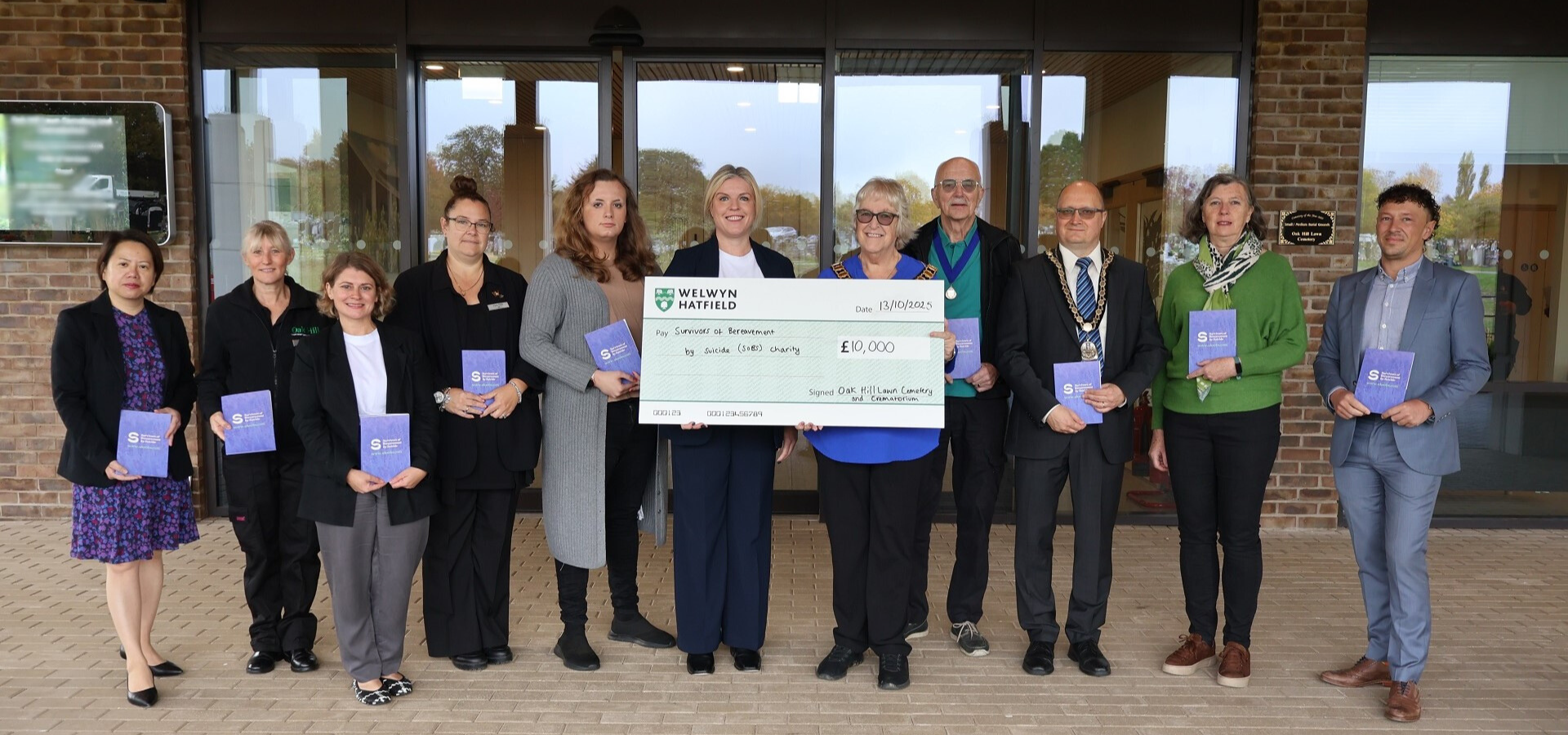 people standing next to someone holding a £10,000 cheque for the soBS charity