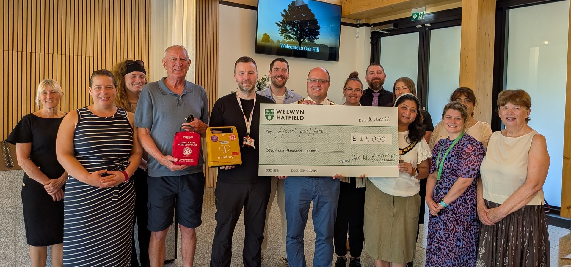 people standing together and one is holding a cheque with the charity heart for herts written on it