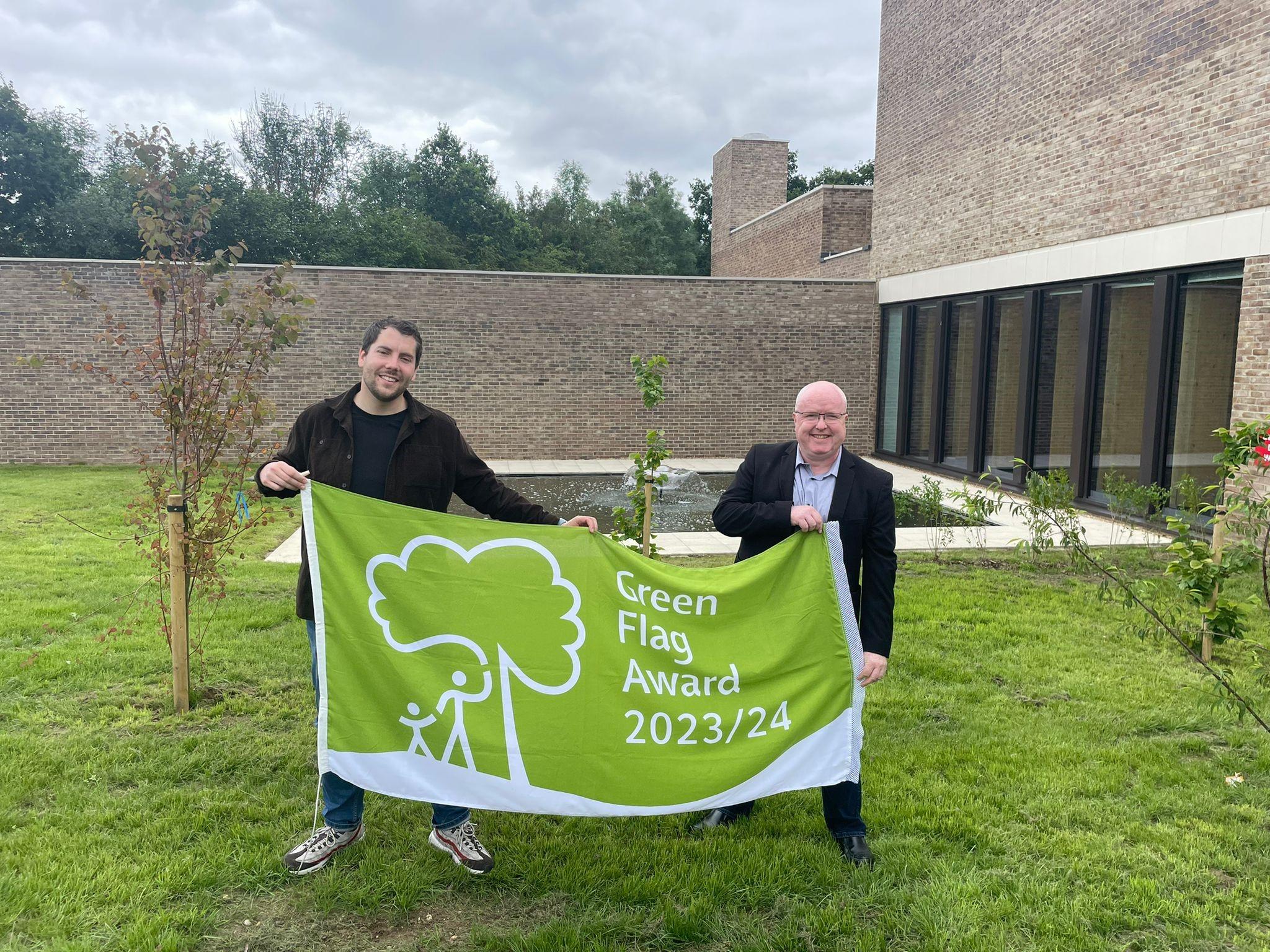 Two men holding up a large green flag.