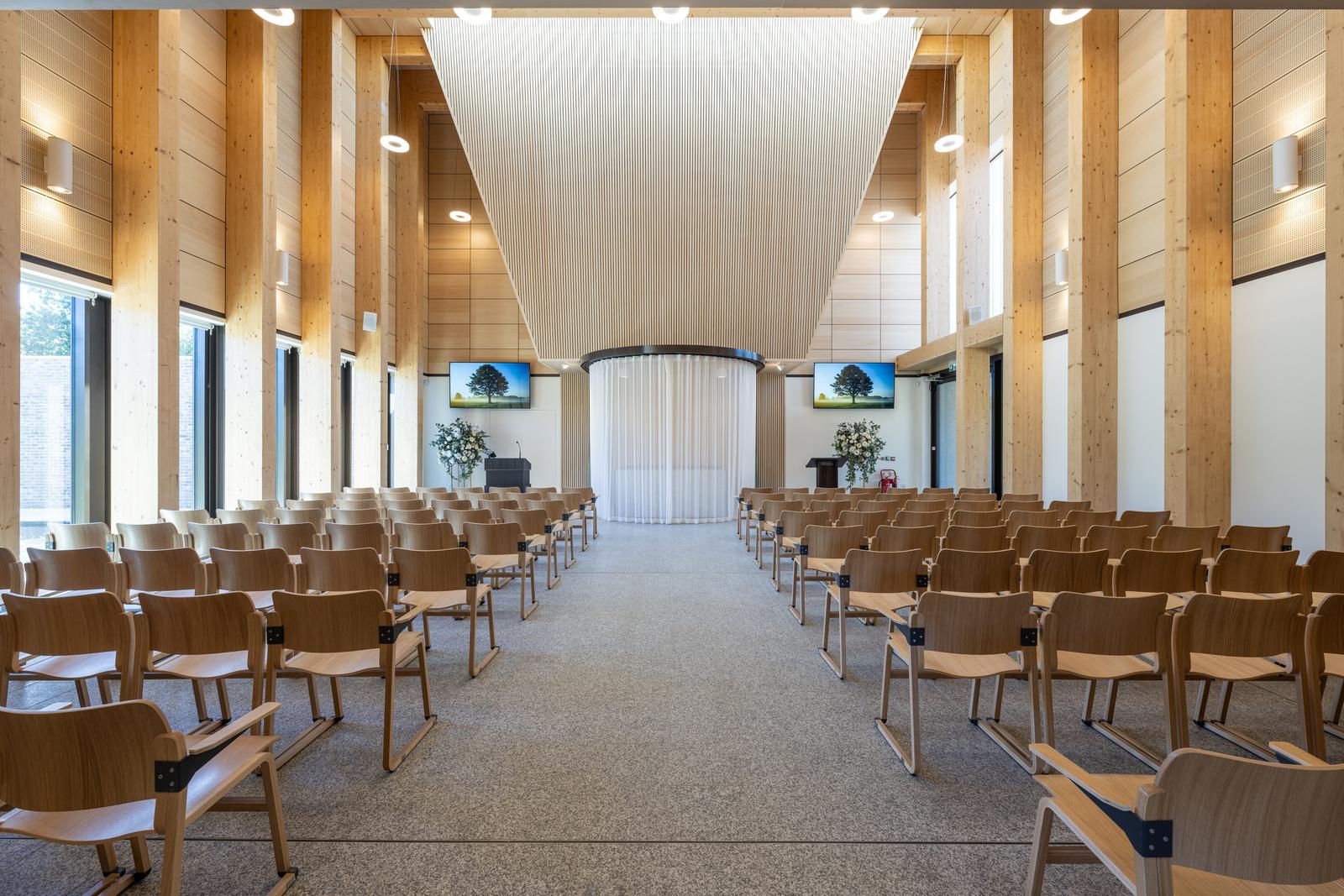 Inside of the chapel where there are wooden chairs and white curtains around a coffin